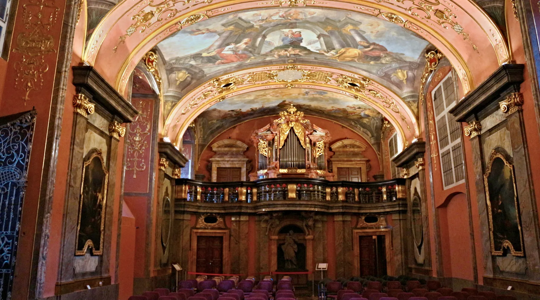The Mirror Chapel from the seating area, with rows of red chairs facing a black and gold organ gallery under a painted vault