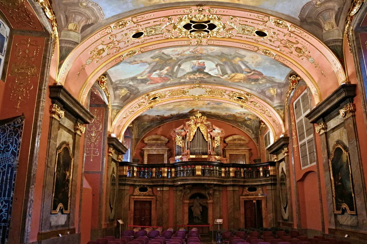 The Mirror Chapel from the seating area: rows of chairs facing a gilded organ gallery under a painted, mirrored vault