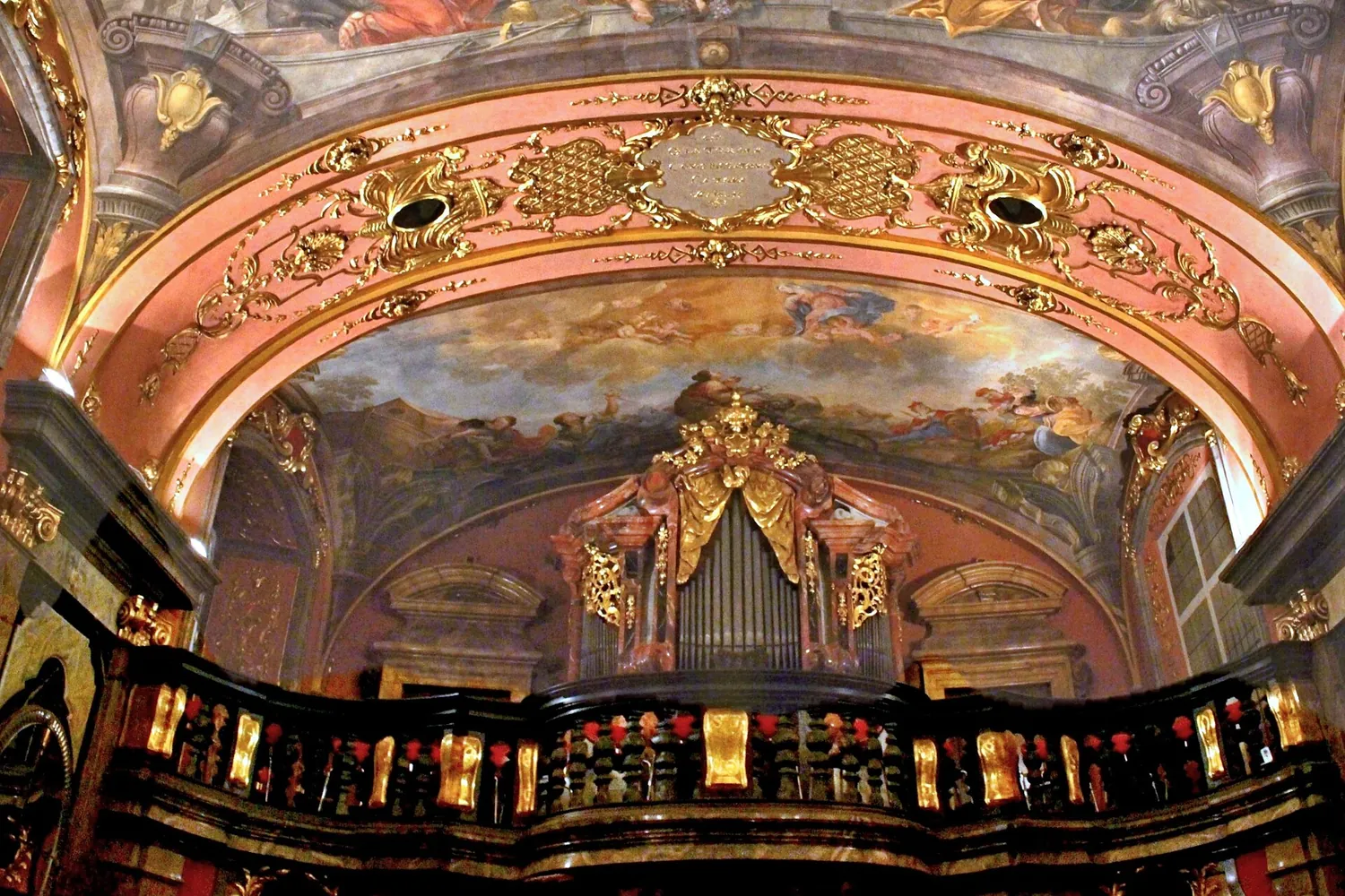 The choir loft of the Mirror Chapel with a black and gold balustrade, a Baroque organ and a painted ceiling above it